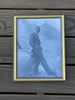 A framed vintage black and white photograph Sean Connery as James Bond in a suit leaning against a car in a mountain setting.