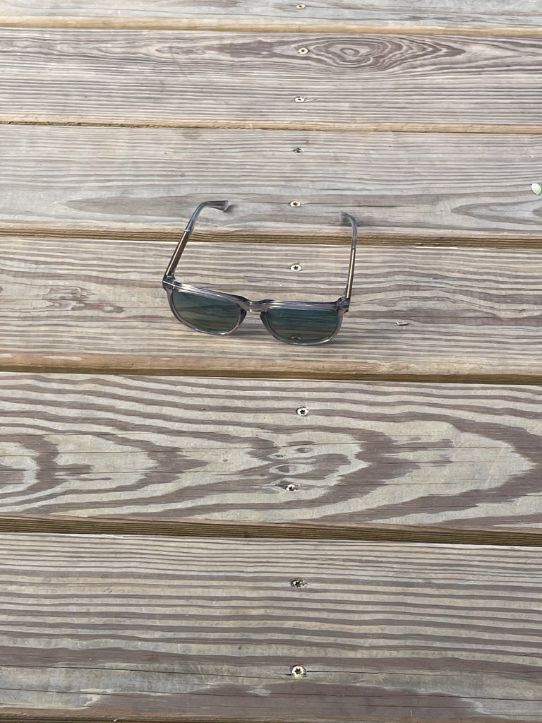 A pair of dark-framed sunglasses with dark lenses resting on weathered wooden planks.
