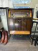 1954 Fonovox, West Germany manufactured,  radio cabinet with a dark brown wood finish, gold-tone metal trim, and silver dials, set in a room with a wood floor.