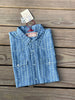 A folded light blue short sleeve chambray shirt with a white vertical stripe pattern, laid flat on a wooden plank surface. It features a button-down front, two buttoned chest pockets, and a red neck label along with a paper tag attached at the collar.