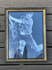 A framed black and white photo print of a guitarist, Pete Townsend, in motion, mounted on a dark wood plank background. The print features a blue tint and is enclosed in a double-matted frame with a gold inner border and a black outer frame.