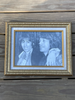A framed monochrome portrait print of Rolling Stones members Mick and Keith, set in an ornate gold frame and mounted against a weathered wooden plank wall.